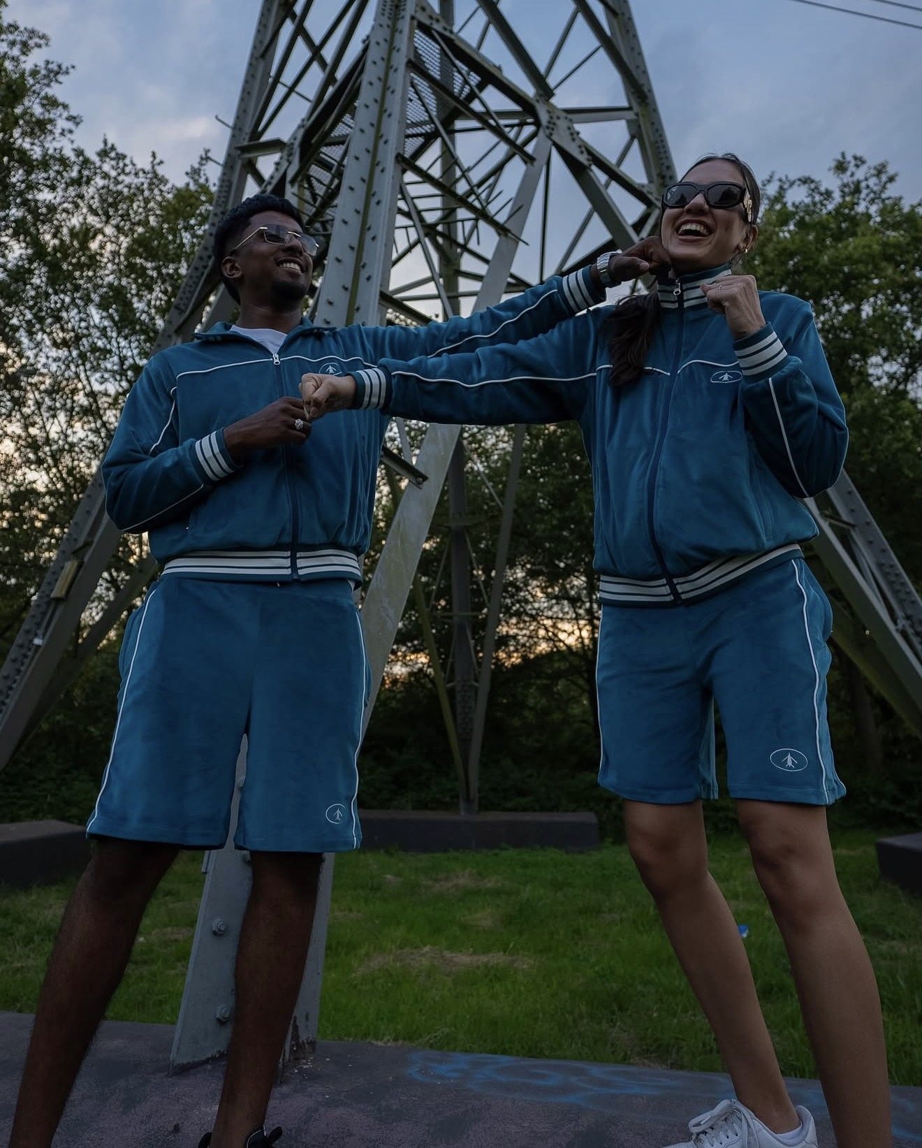 Zwei Models im blauen Velours-Trainingsanzug unter einem Strommast